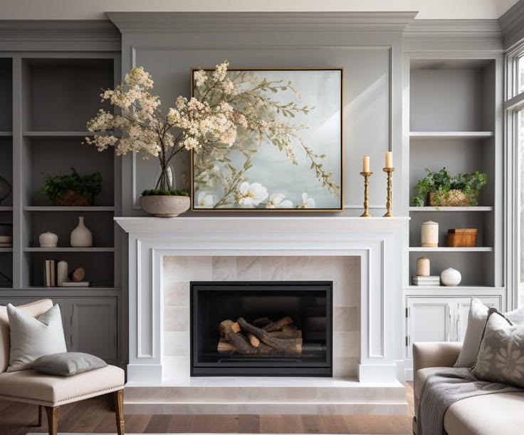 Pale grey panelled sitting room with a marble chimneypiece, built-in shelving and blossom in a stone urn