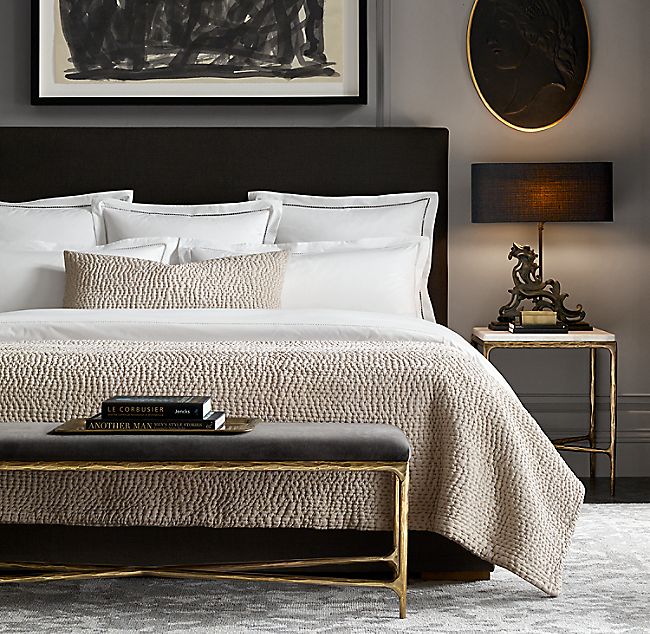 Dark neutral bedroom with layered natural bedding and restrained brass details