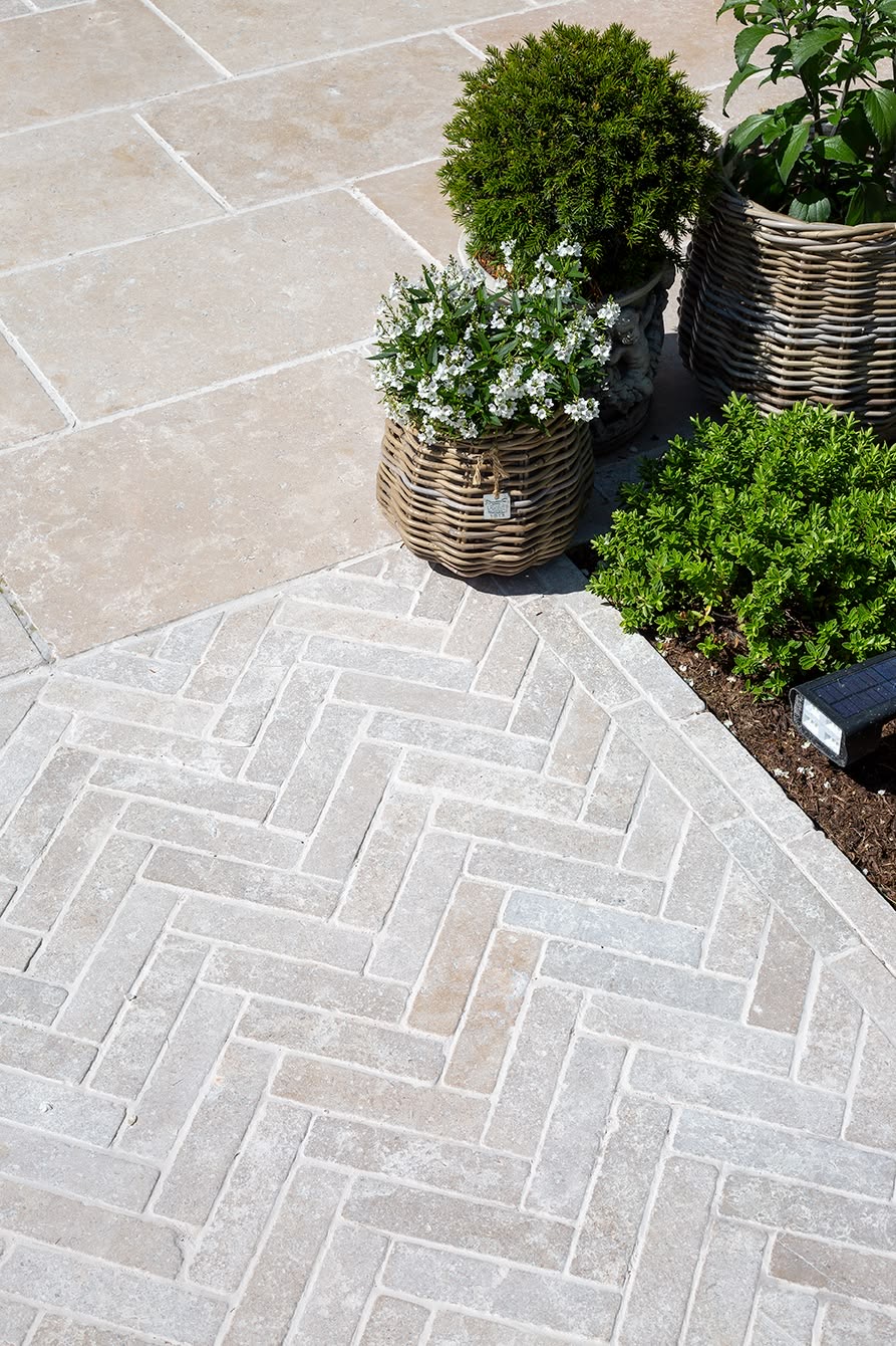 Carefully laid herringbone paving meeting stone terrace and planted borders